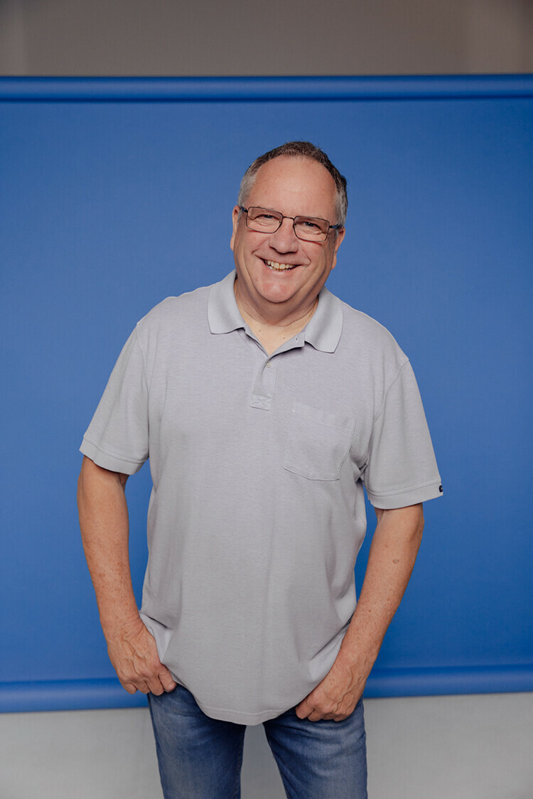 Por trait of middle aged man standing in front of blue backdrop smiling