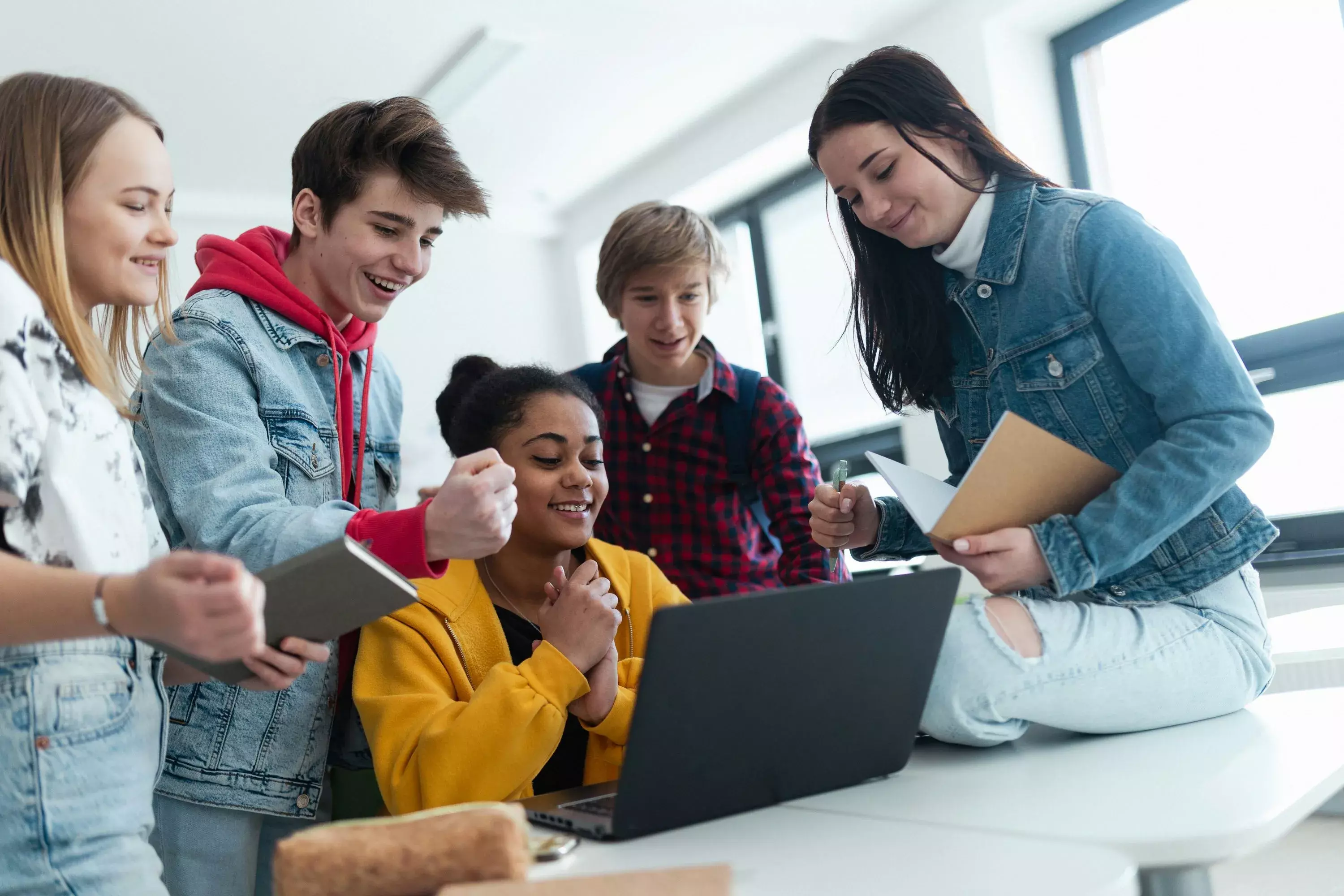 Group of students gathered around a laptop collaborating on a project in a classroom.