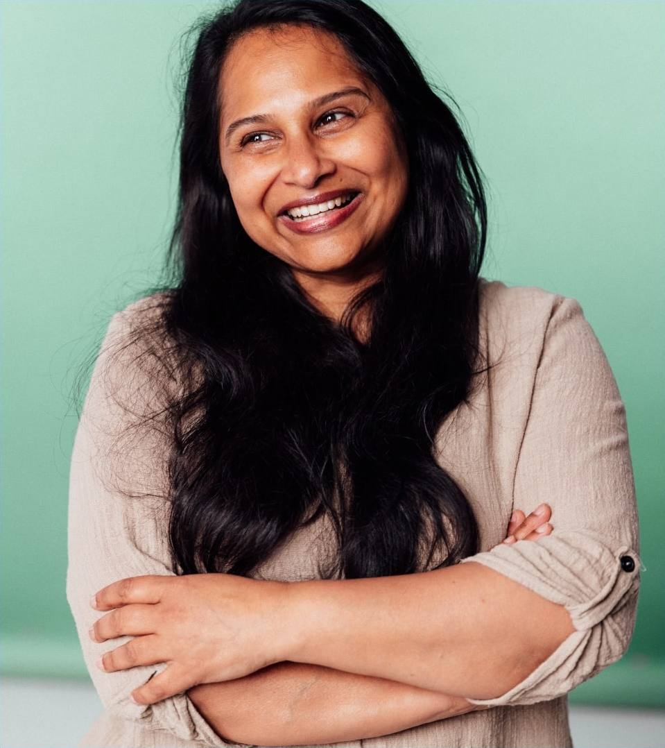 Woman with long dark hair smiling with her arms crossed against a green background.