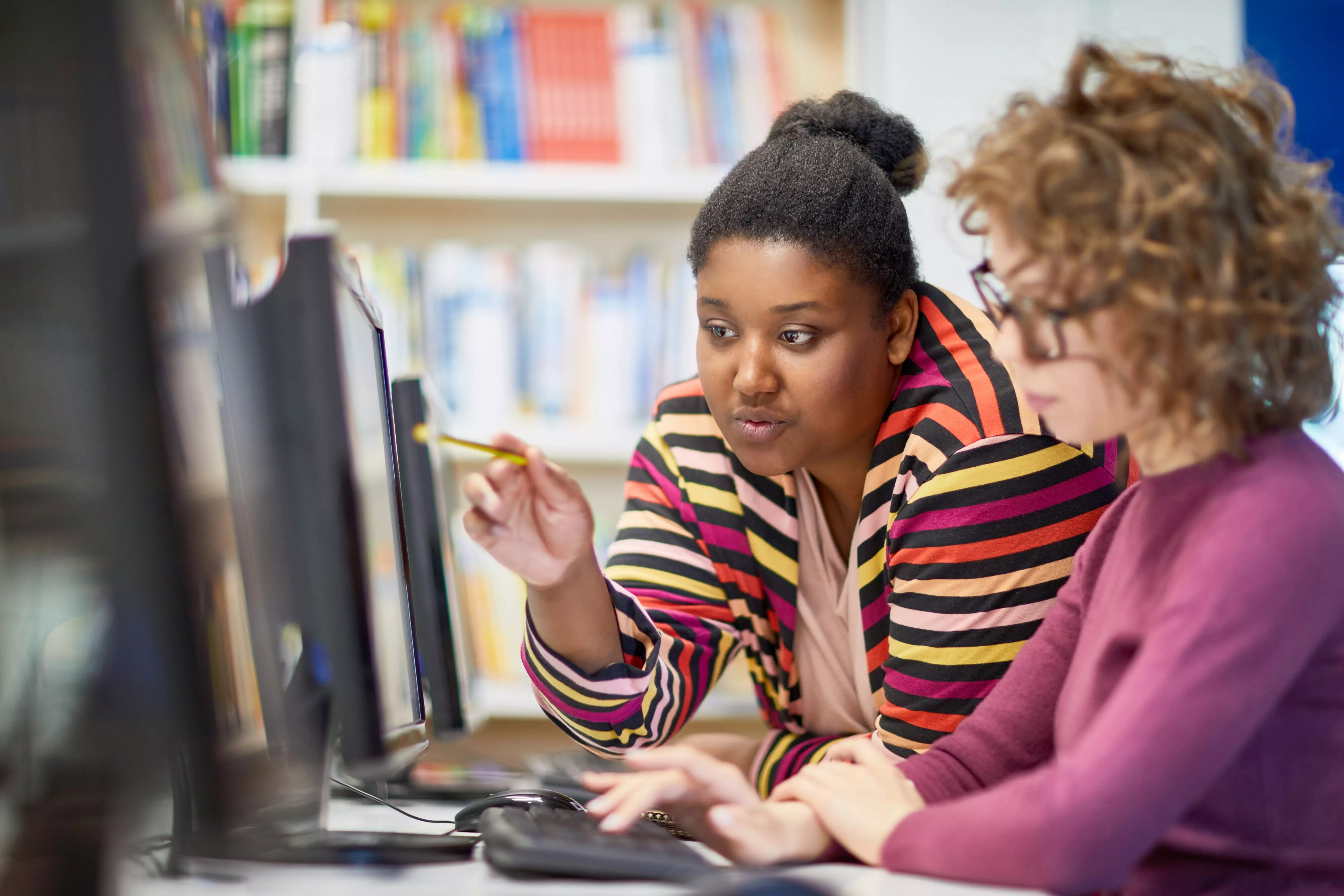A young teacher pointing at a computer monitor, assisting student.